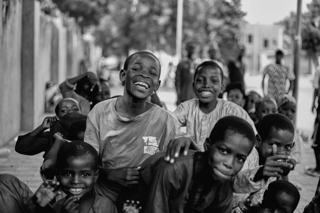 Black and white photo of smiling African children playing joyfully outdoors, capturing youthful energy.