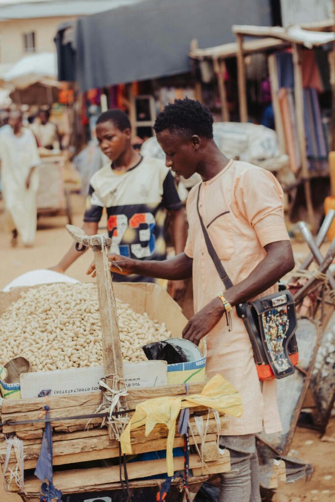 Young man sells peanuts at an outdoor street market, engaging with customers.